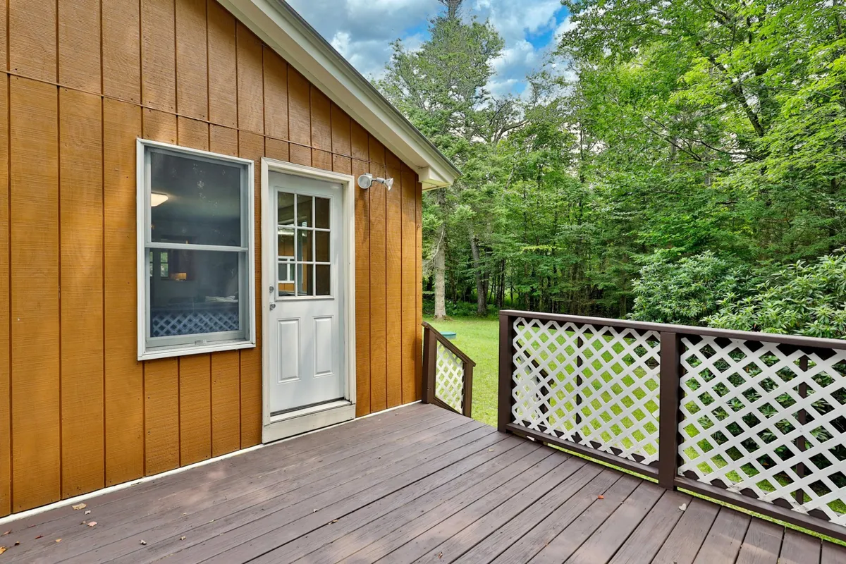 A welcoming wooden deck with a white door opens out onto lush green foliage, providing a seamless transition from indoors to the outdoors. The space is ideal for hosting family gatherings, enjoying morning coffee, or playing outdoor games, all while basking in the fresh mountain air.