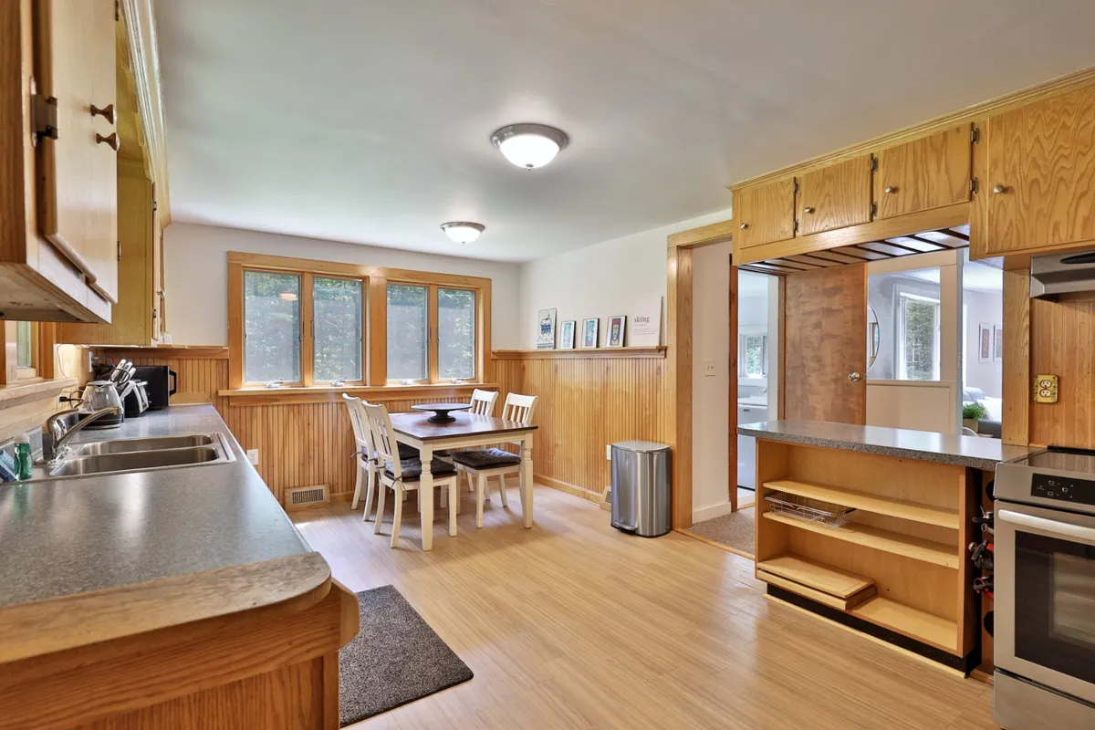 A warm and inviting dining area sits adjacent to a well-equipped kitchen counter. Large windows provide natural light, while the dining table is set to accommodate group meals and family gatherings. The space strikes a balance between rustic charm and modern convenience, with subtle decor touches that reinforce a homey vibe.