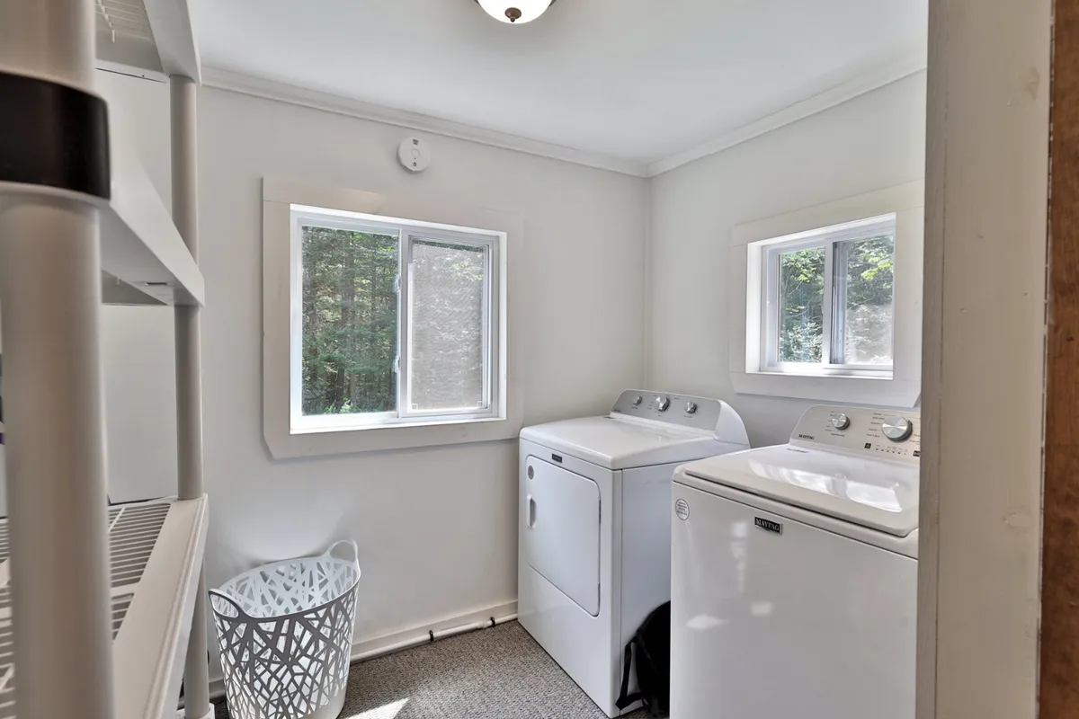 A well-organized laundry room featuring a washing machine, dryer, bright windows, and a laundry basket. The space is functional, tidy, and filled with natural light, emphasizing everyday convenience.