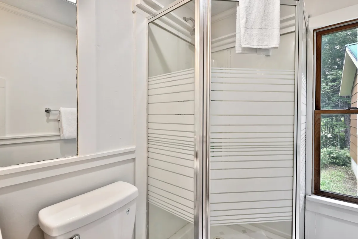 A bright bathroom with a glass shower enclosure, white towels neatly hung, a toilet, and a window letting in natural light. The space feels clean, modern, and serene—ideal for unwinding after a day outdoors.