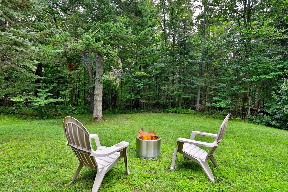 A cozy fire pit area ringed by classic Adirondack chairs, nestled among tall trees. The atmosphere is inviting and serene, ideal for evening gatherings, campfire storytelling, or roasting marshmallows under the stars.