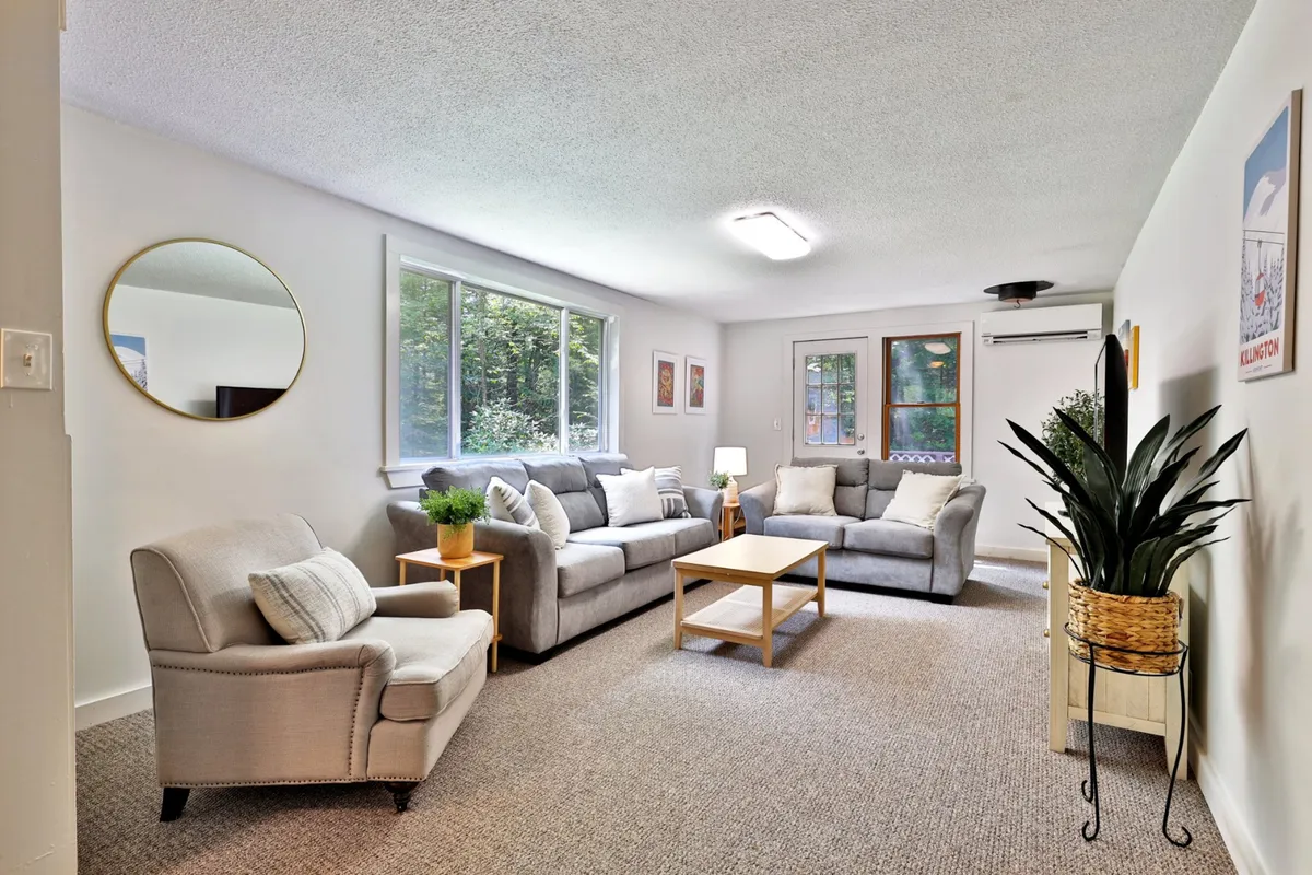 This inviting interior scene showcases a cozy living room with a plush sofa set, a rustic coffee table, a vibrant potted plant, and tasteful decorative wall art. The space is bathed in natural light, creating a warm, welcoming atmosphere perfect for relaxing, socializing, or enjoying quiet moments with a book or a hot drink.