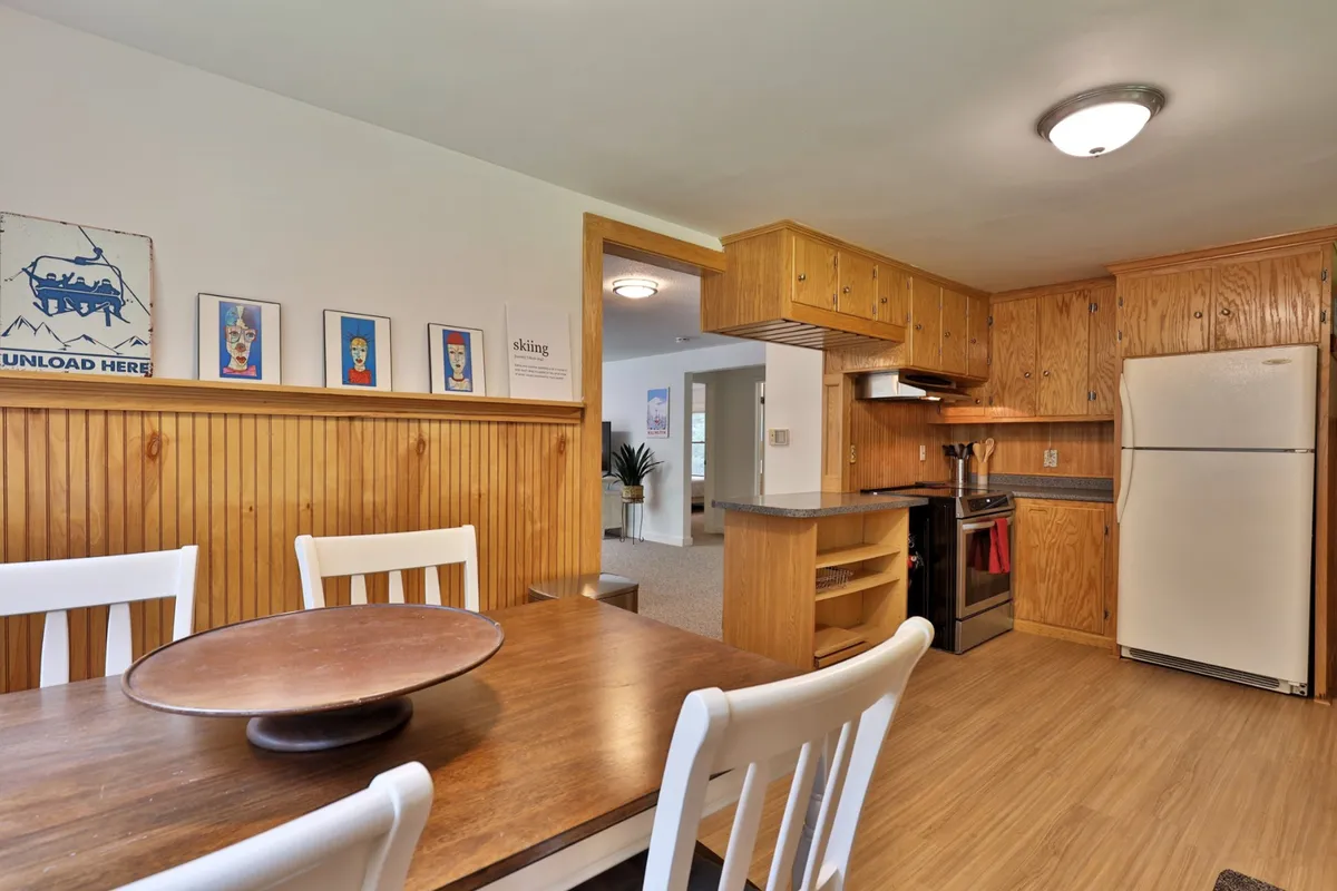 A cozy and inviting view of the dining table adjacent to the kitchen area, with wooden cabinetry and wall art adding warmth. The space is designed for entertaining guests, sharing meals, or enjoying downtime with family or colleagues.