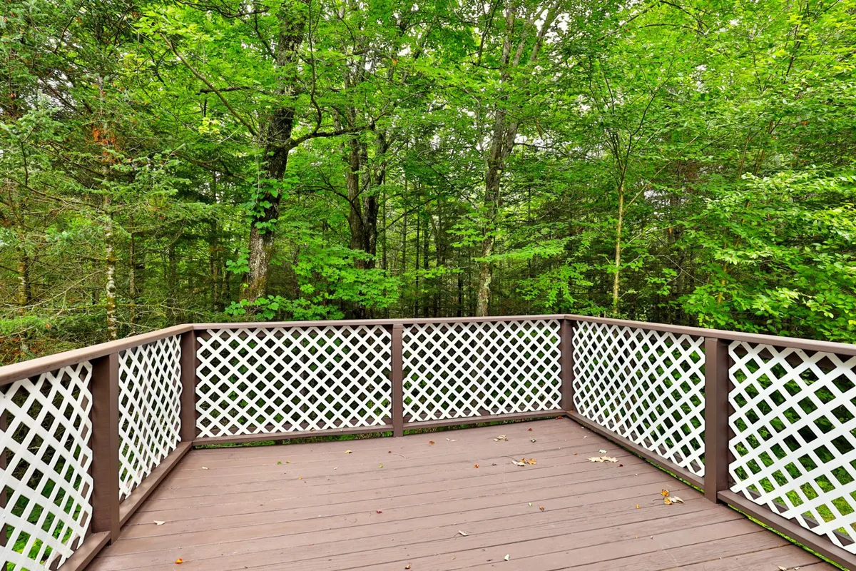 A spacious wooden deck with lattice railings overlooks lush greenery, offering a tranquil setting surrounded by nature. The area is perfect for relaxing, reading, or enjoying the outdoors, with ample space for family and pets to gather. The deck's elevated position hints at scenic views and a connection to the surrounding environment.