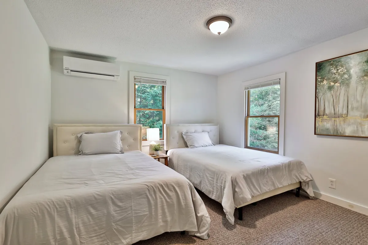 A serene interior with two beds, a decorative painting, and windows letting in soft light. The arrangement suggests a restful space for both people and pets to unwind after exploring. The windows help maintain a sense of connection between the home and the outside environment.