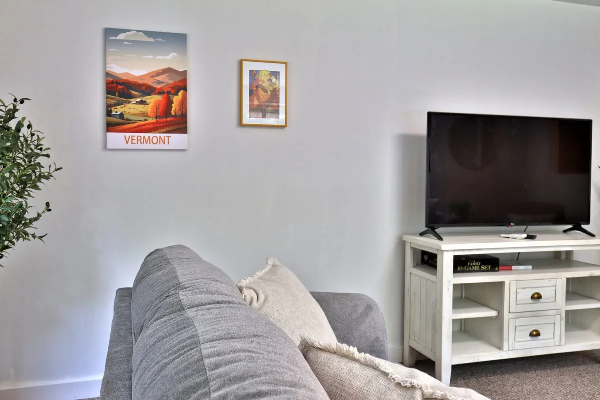 A lounge area featuring a Vermont poster, framed artwork, a TV, and a comfortable couch. The mood is cozy, with elements that imply a sense of personalized, secure, and well-cared-for home environment.