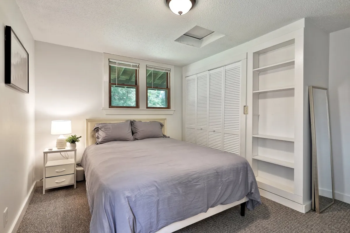 A serene bedroom scene with a comfortable bed, soft linens, a nightstand with a lamp, and windows offering soothing natural light. The built-in closet adds convenience and the overall mood is tranquil—ideal for restful mornings or intimate retreats.